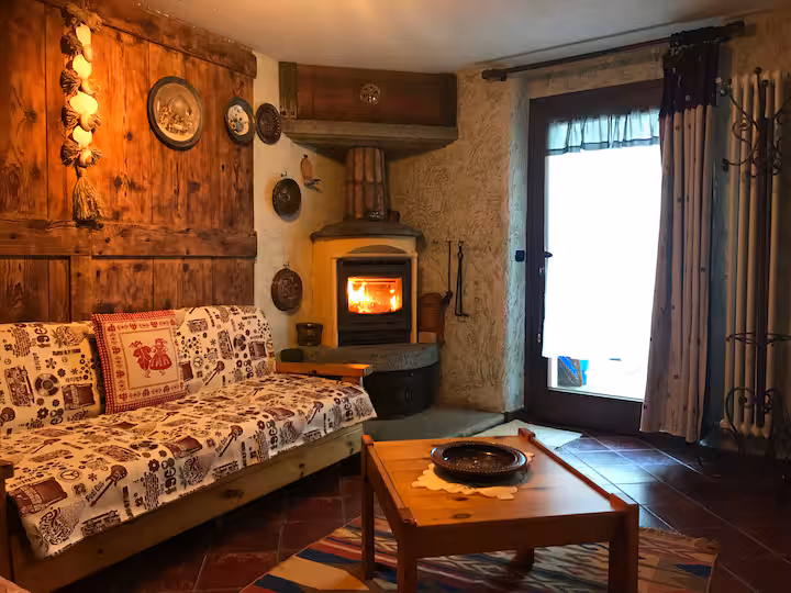 Living room with glowing wood-burning stove, rustic sofa and natural afternoon light