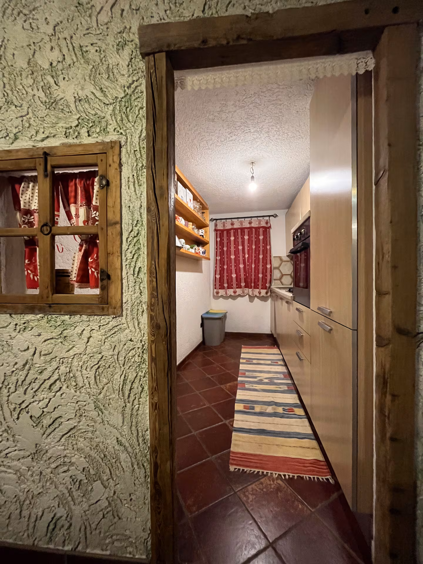 Kitchen viewed through stone arch doorway with red curtains and open shelving
