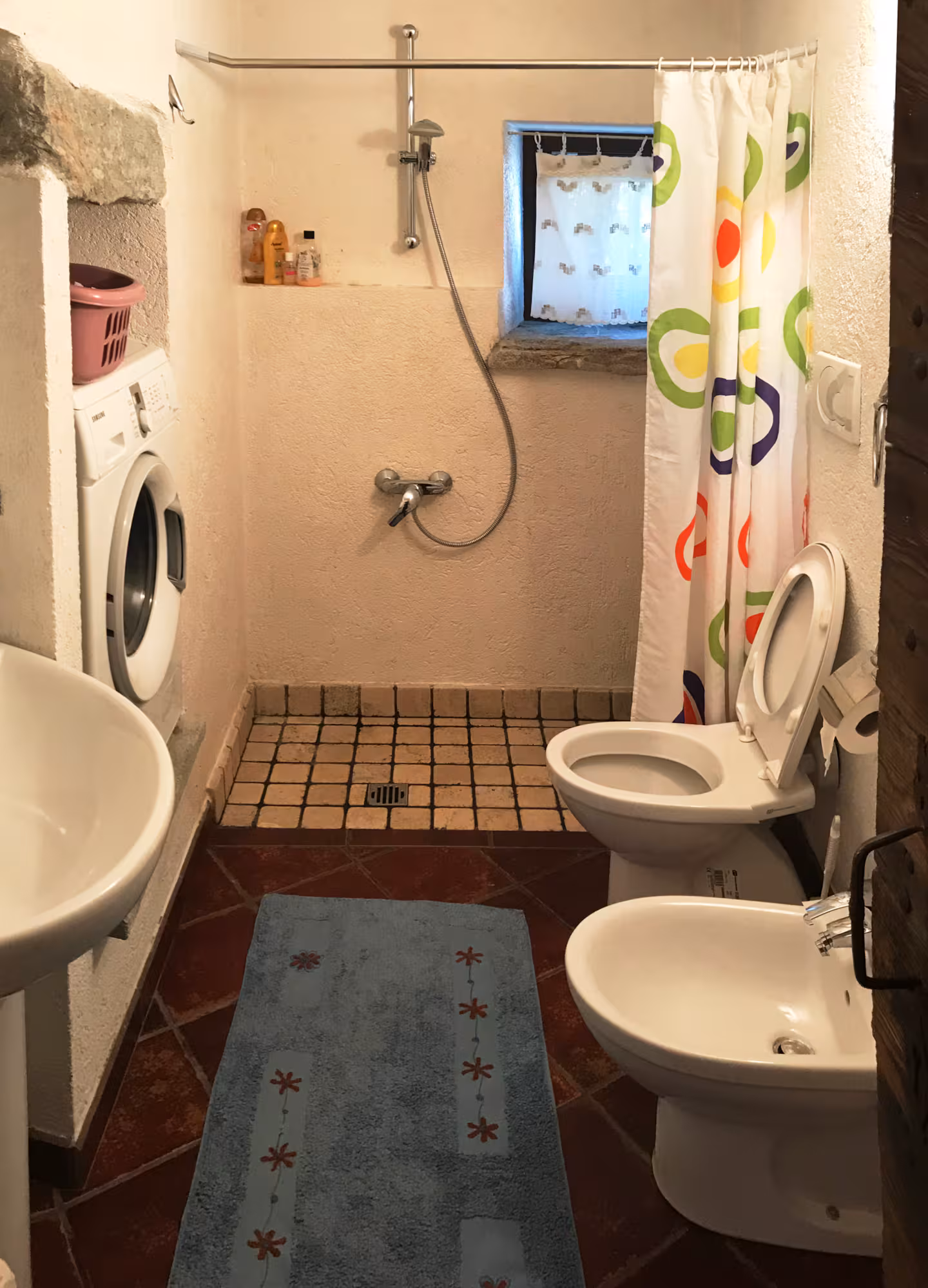 Bathroom with shower, washing machine, bidet and terracotta tile floor