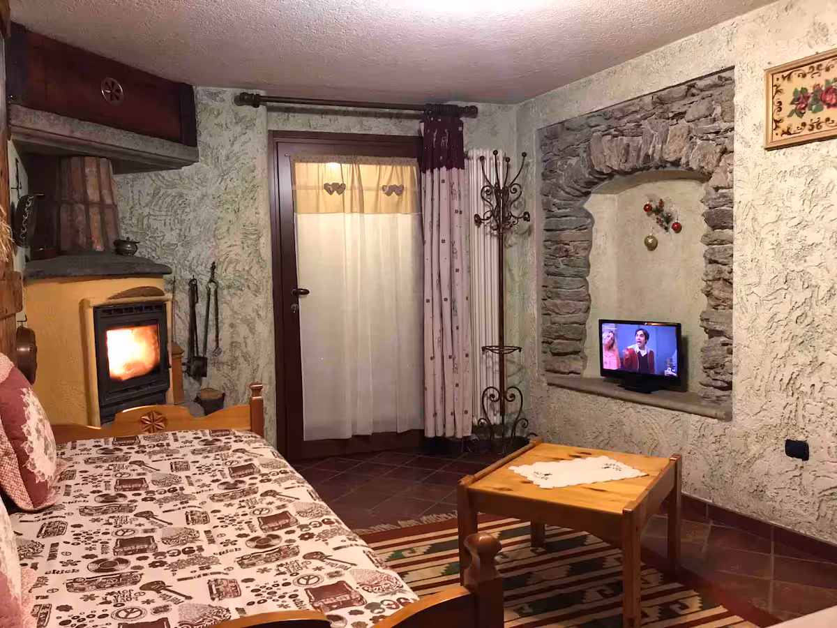 Living area with sofa bed, wood-burning stove, stone walls and TV niche