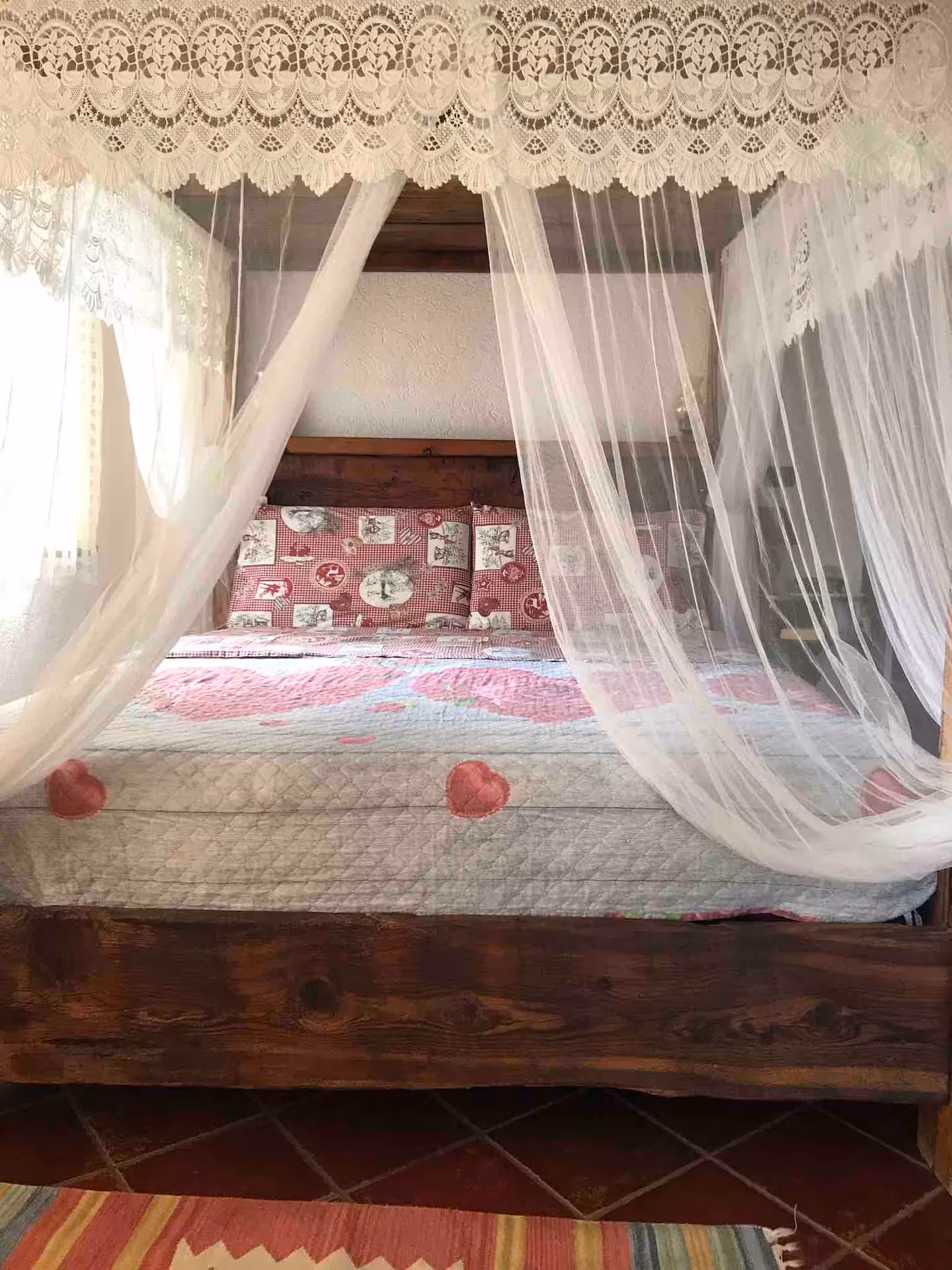 Canopy bed wide view with flowing lace curtains, heart-pattern duvet and woven rug floor